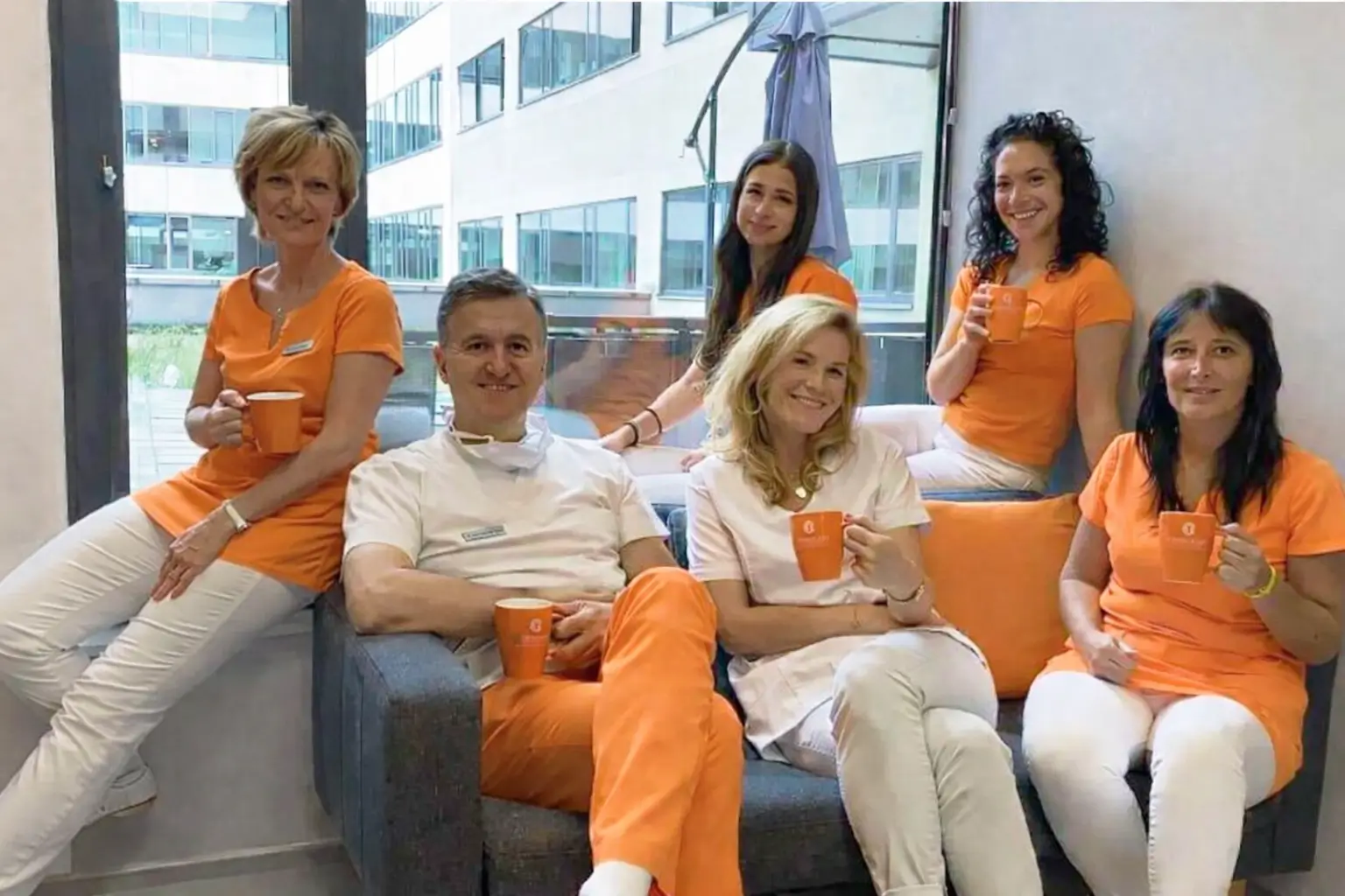 A Czinkoczky Implant csapata narancssárga és fehér munkaruhában egy kanapén ülve, egy modern rendelő közösségi terében.